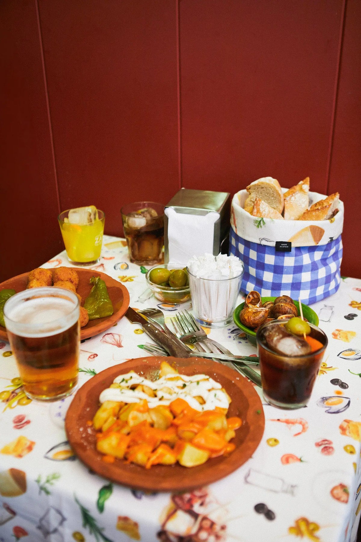 Mantel blanco con estampado de ilustraciones coloridas de comida sobre una mesa llena de platos de tapas y bebidas.