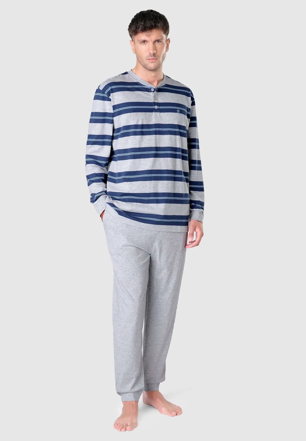 Modelo con pijama de hombre: camiseta de rayas azules y grises con botones y pantalón gris liso de punto.
