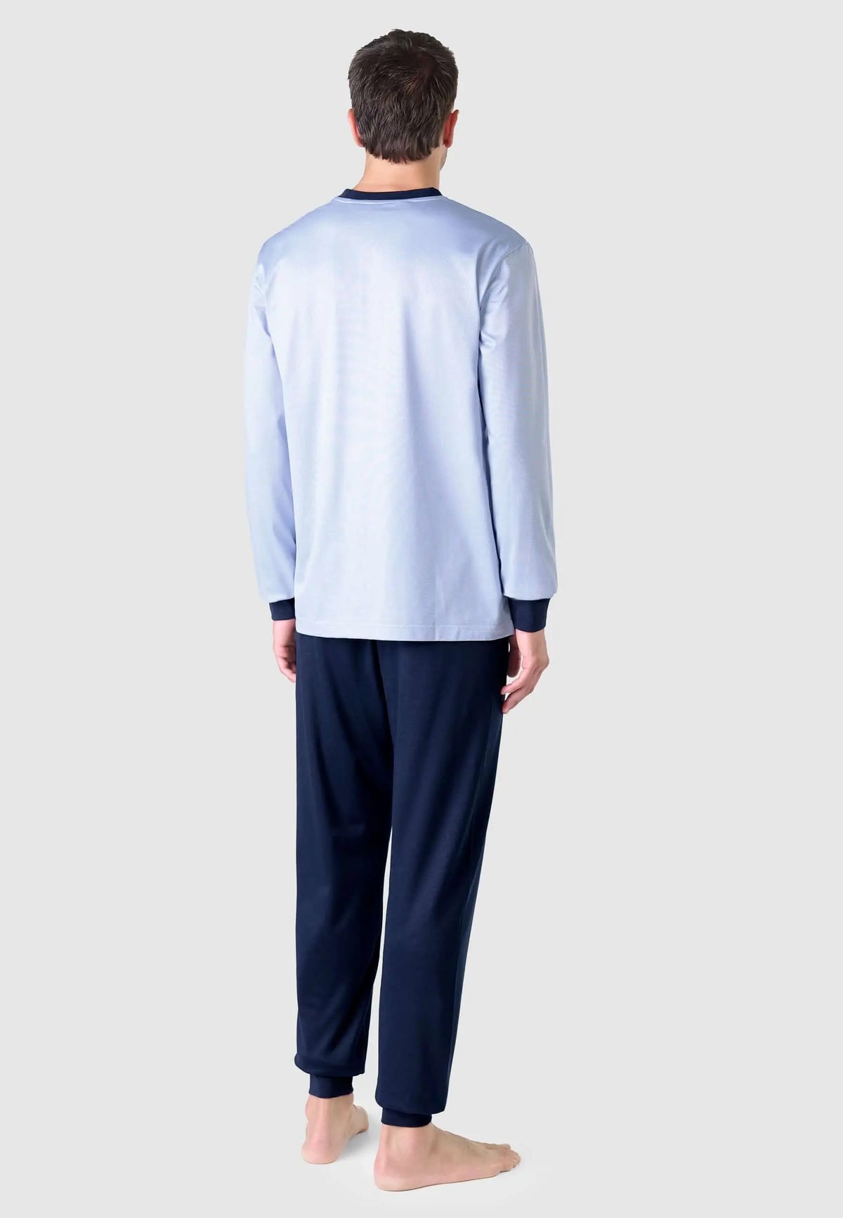 Hombre de espaldas vistiendo pijama largo azul claro de manga larga con puños y pantalón azul marino liso.