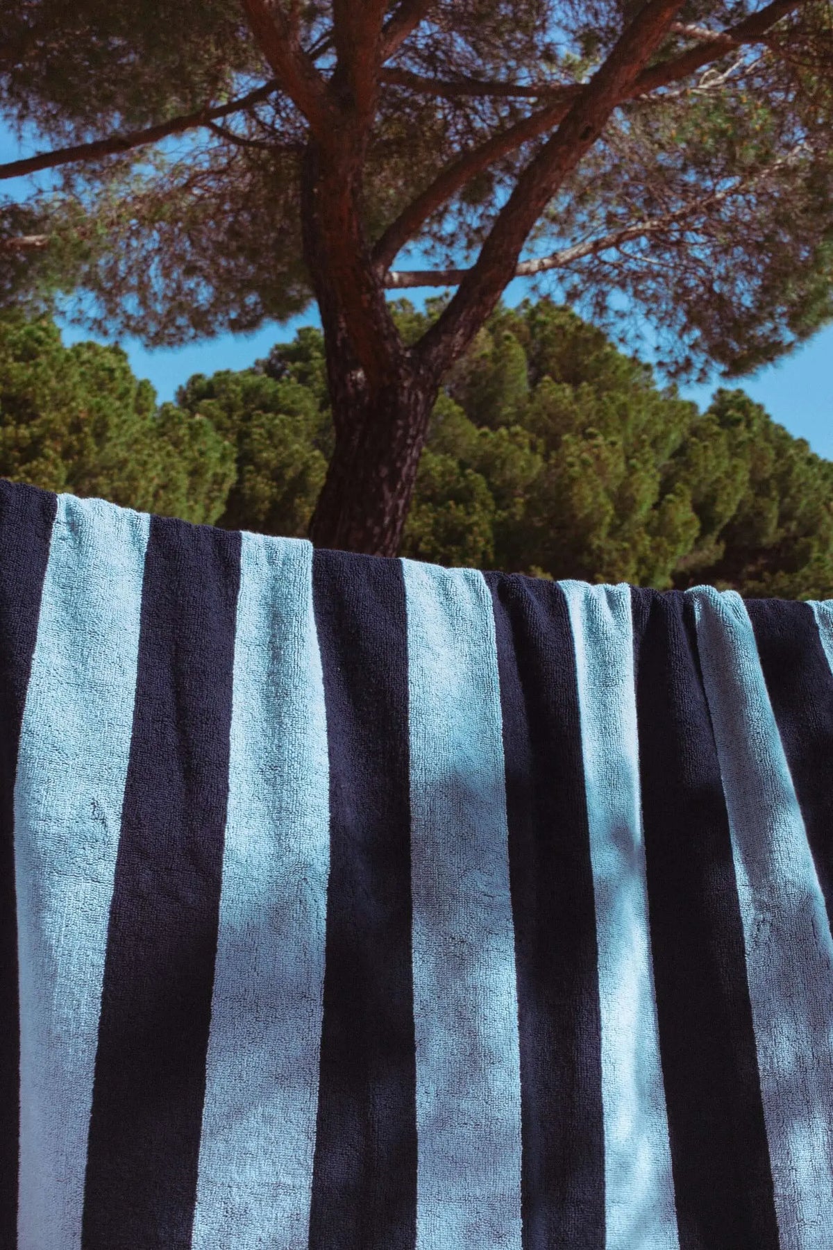 Navy blue and light blue striped beach towel hanging outdoors with trees in the background.