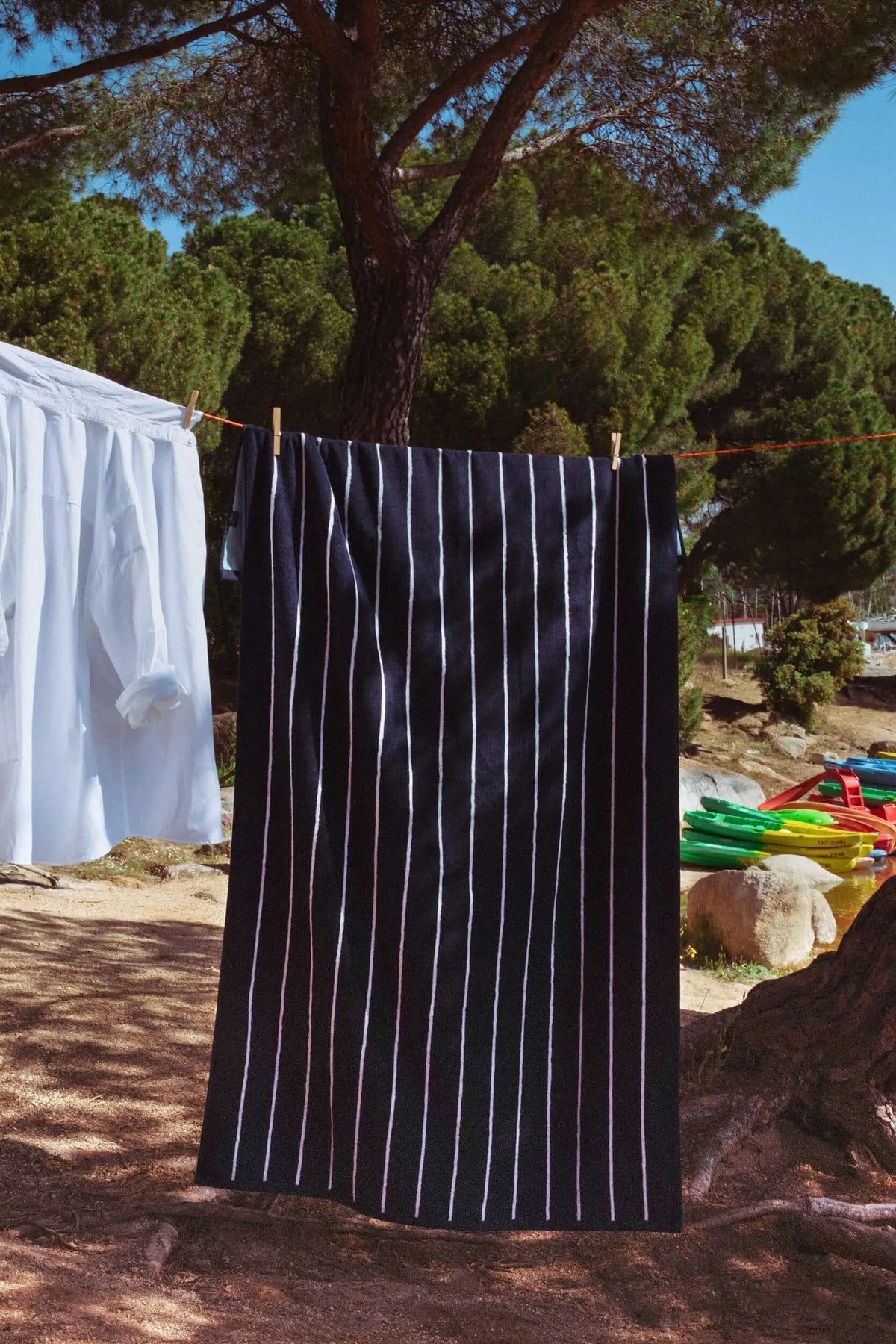Rectangular navy blue beach towel with thin light blue vertical stripes, hanging on a clothesline outdoors.