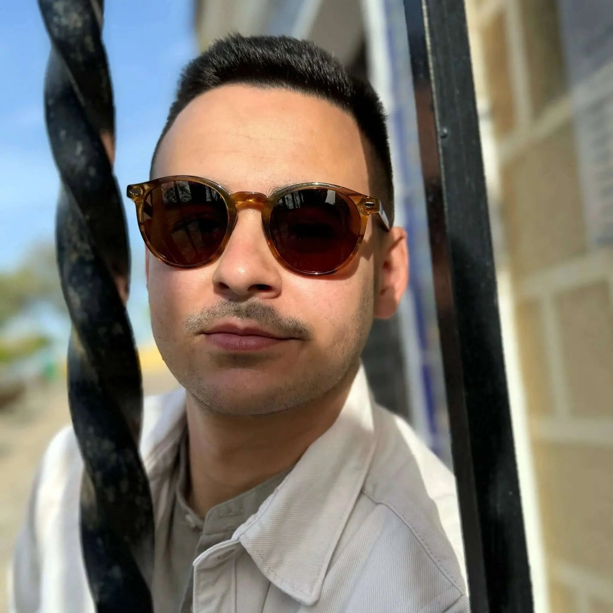 Hombre con gafas de sol redondas de montura color naranja cristal y lentes marrones oscuras, estilo casual al aire.