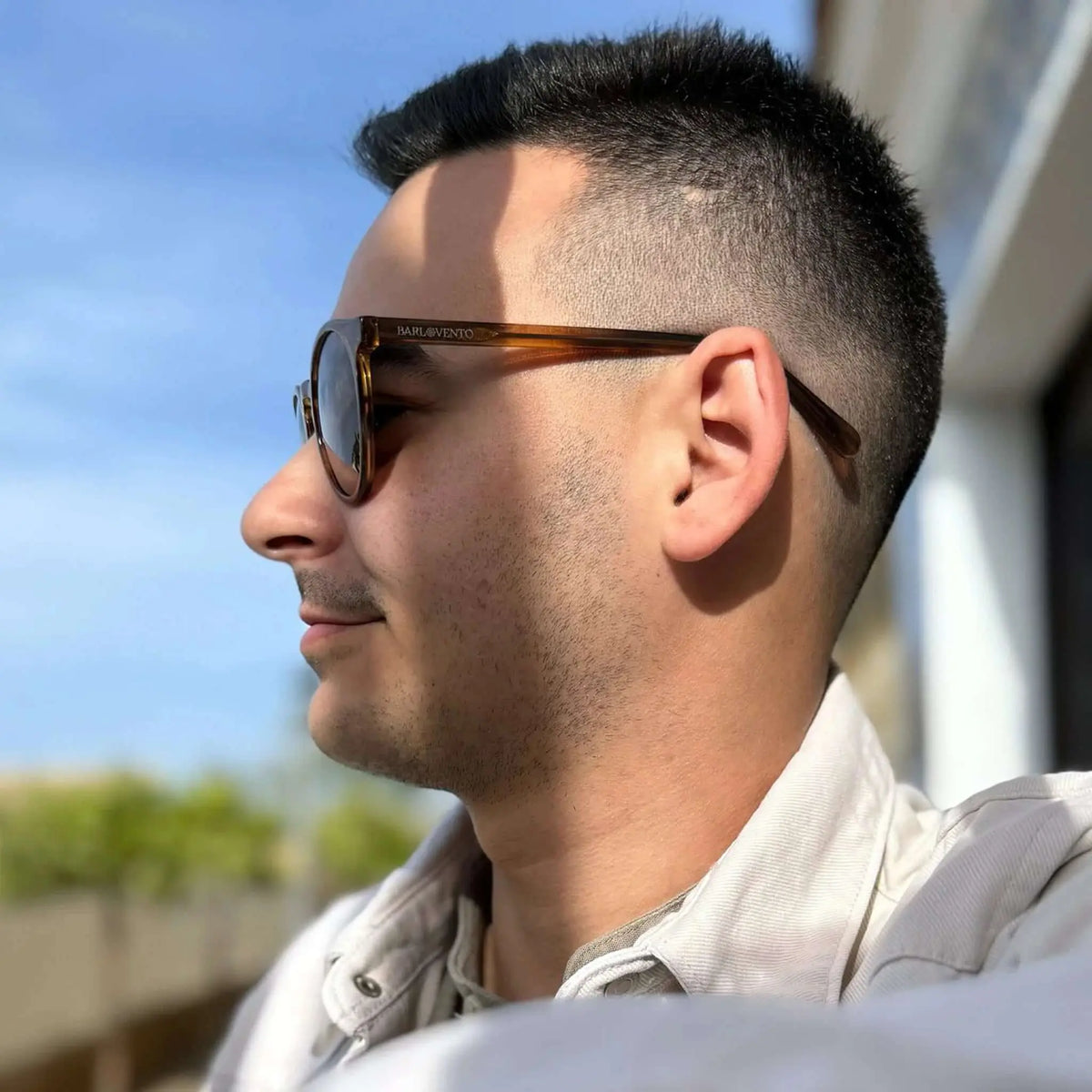 Hombre con gafas de sol redondas de acetato naranja cristal y lentes marrones, estilo casual en exterior soleado.