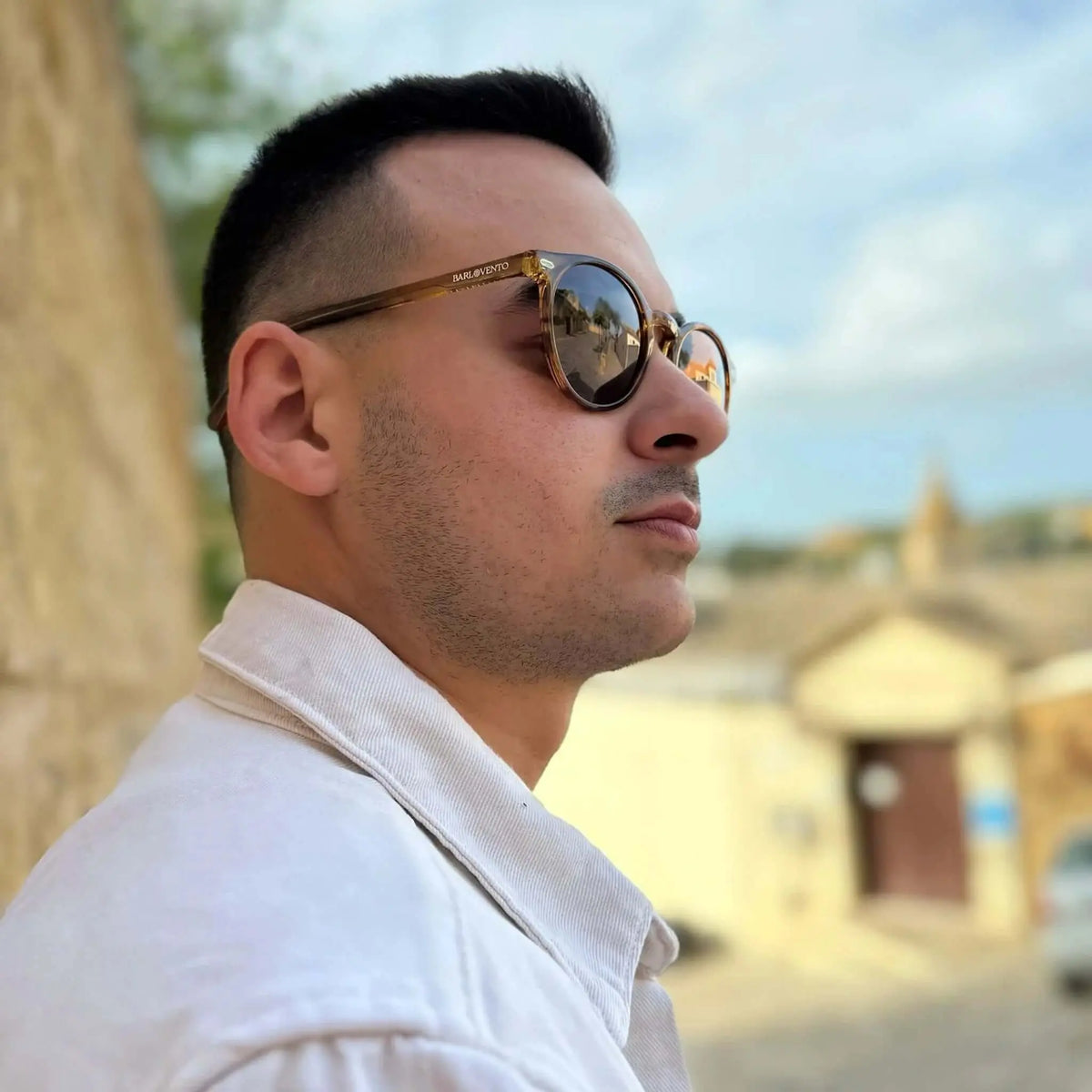 Hombre con gafas de sol redondas de acetato naranja cristal y lentes marrones, estilo casual en exterior.