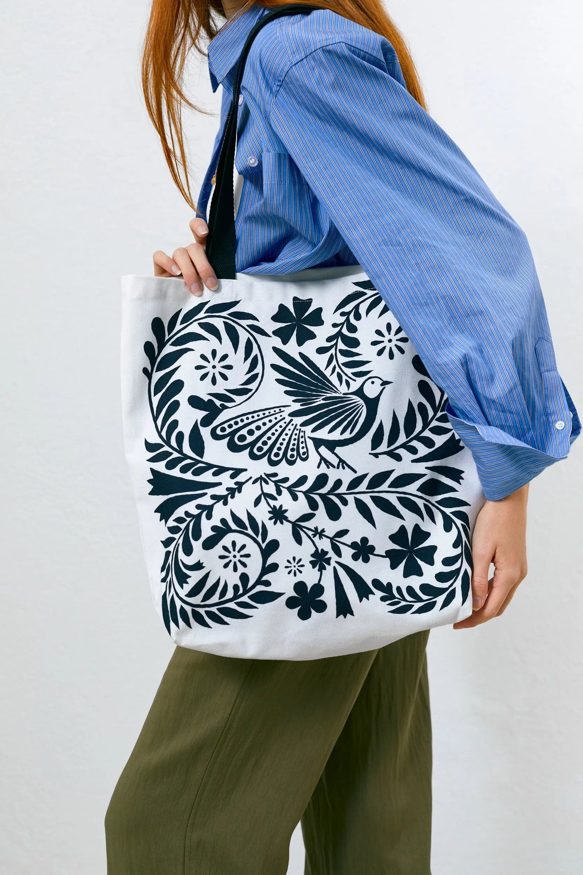 Tote bag de tela blanca con estampado botánico y de aves en color azul oscuro, con asas negras.