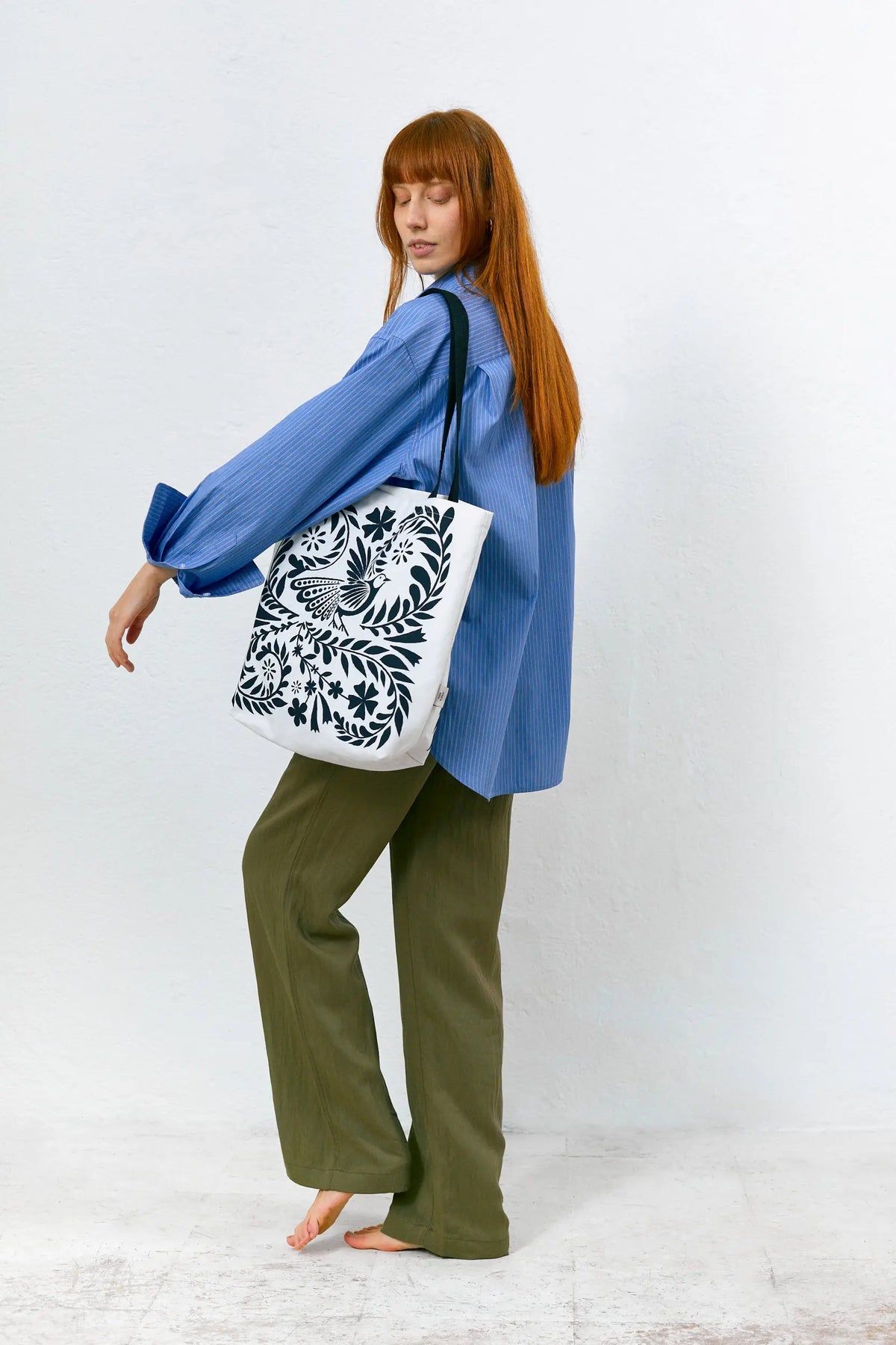 Tote bag blanca de tela con diseño floral y de aves en azul oscuro, con asas negras largas para colgar al hombro.
