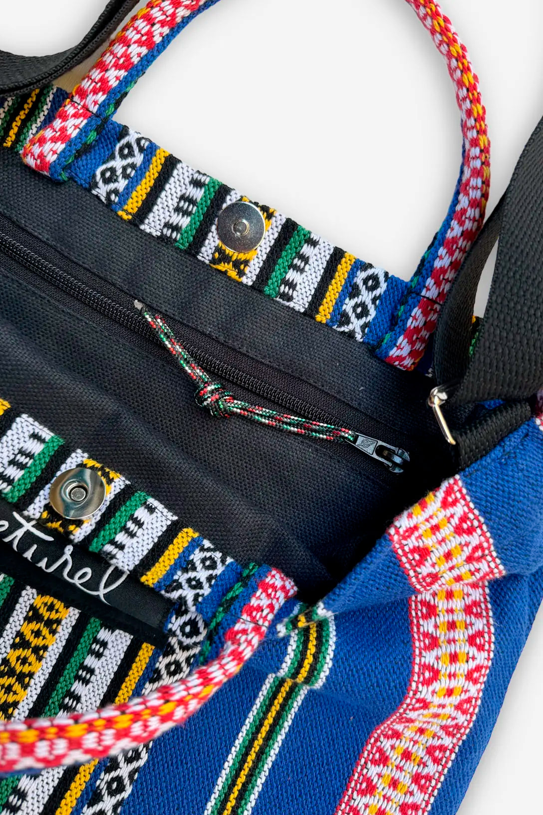 Bolso bandolera de lona azul con tejido étnico multicolor, cierre de cremallera y botón magnético de metal.