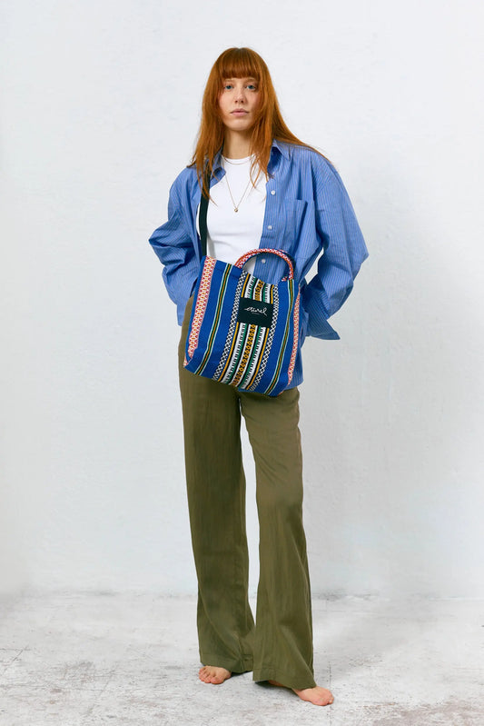 Blue fabric crossbody tote bag with vertical stripes, geometric patterns, red accents, and a top handle.