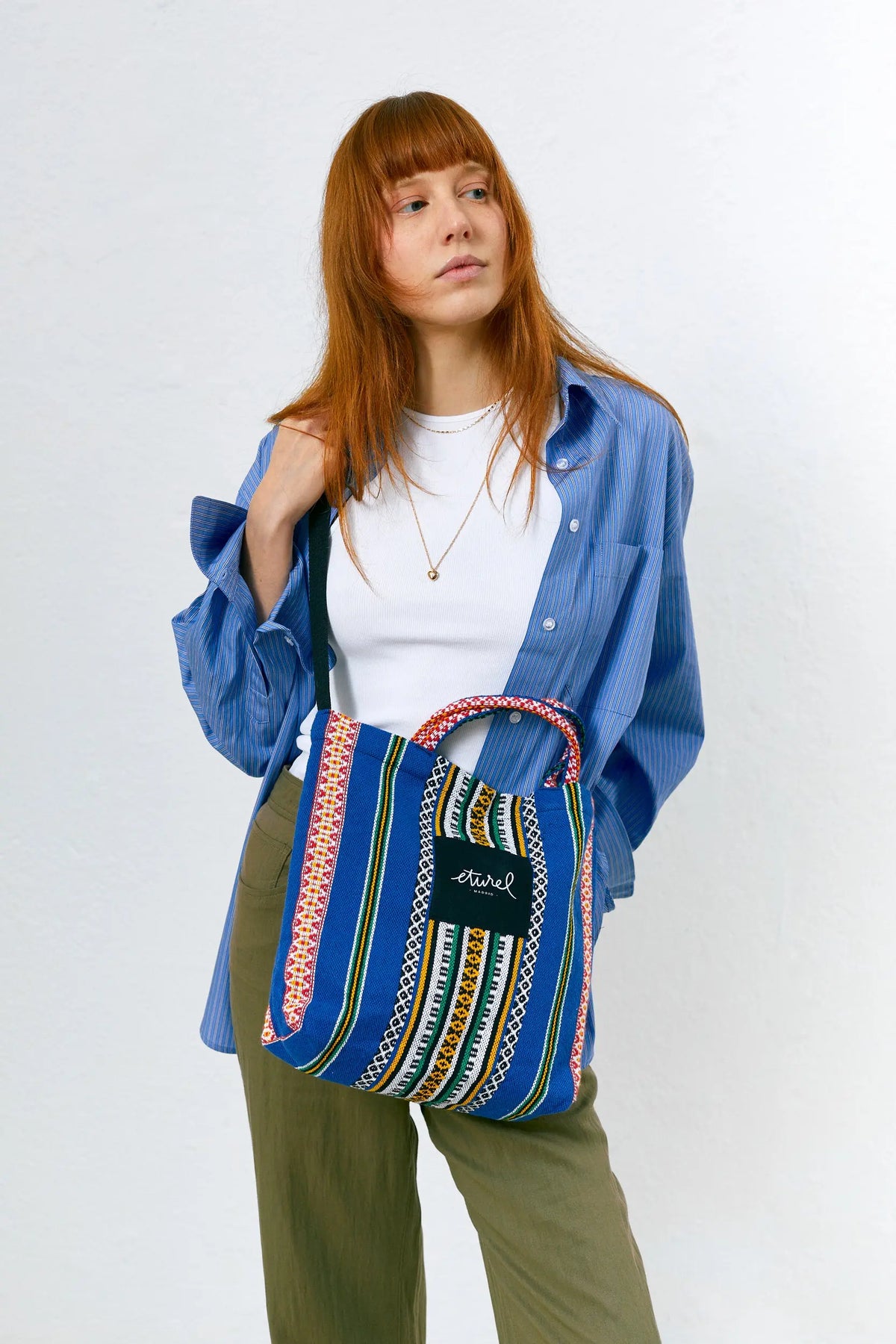 Bolso bandolera tipo tote de tela azul con estampado geométrico multicolor y asas cortas, llevado cruzado por una mujer.