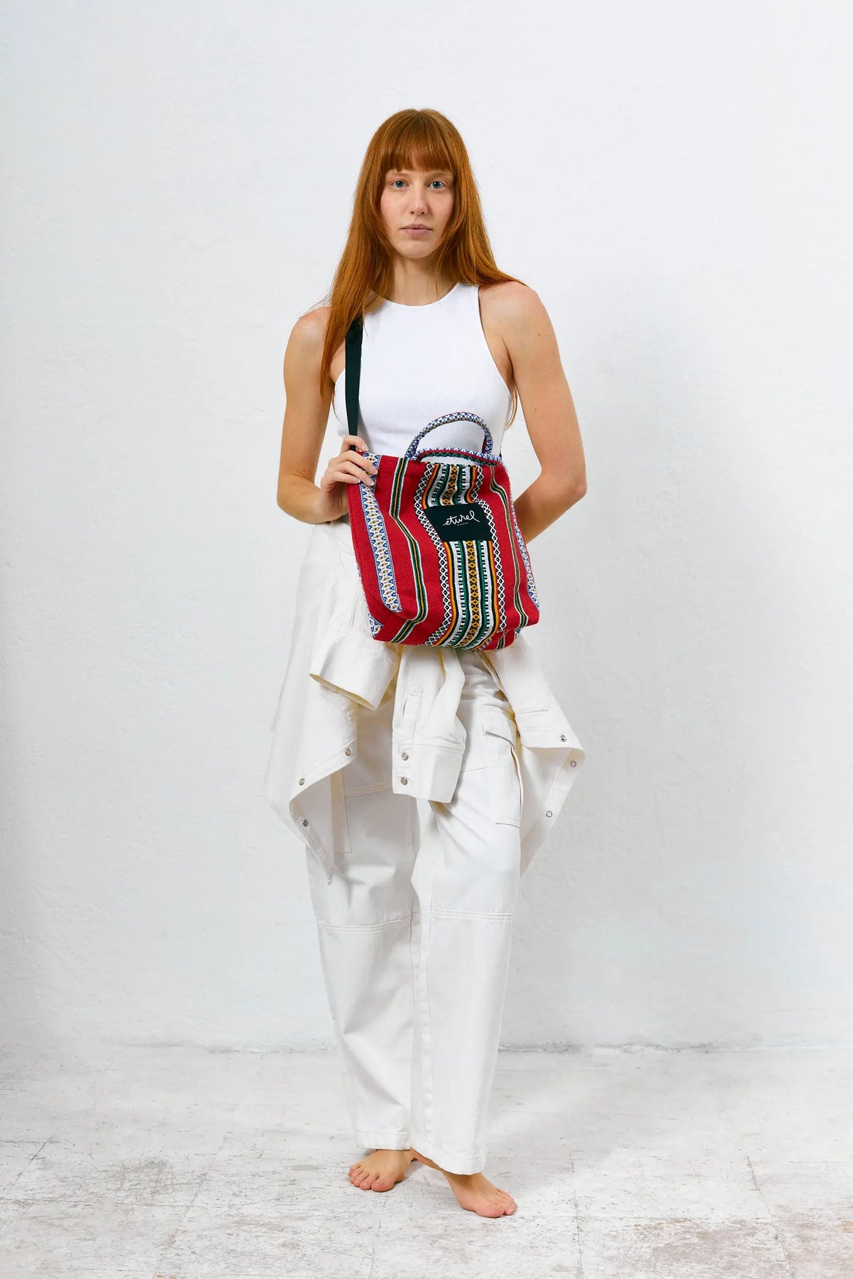 Bolso bandolera rojo de tela con estampado étnico, forma rectangular, asas cortas y correa negra cruzada.