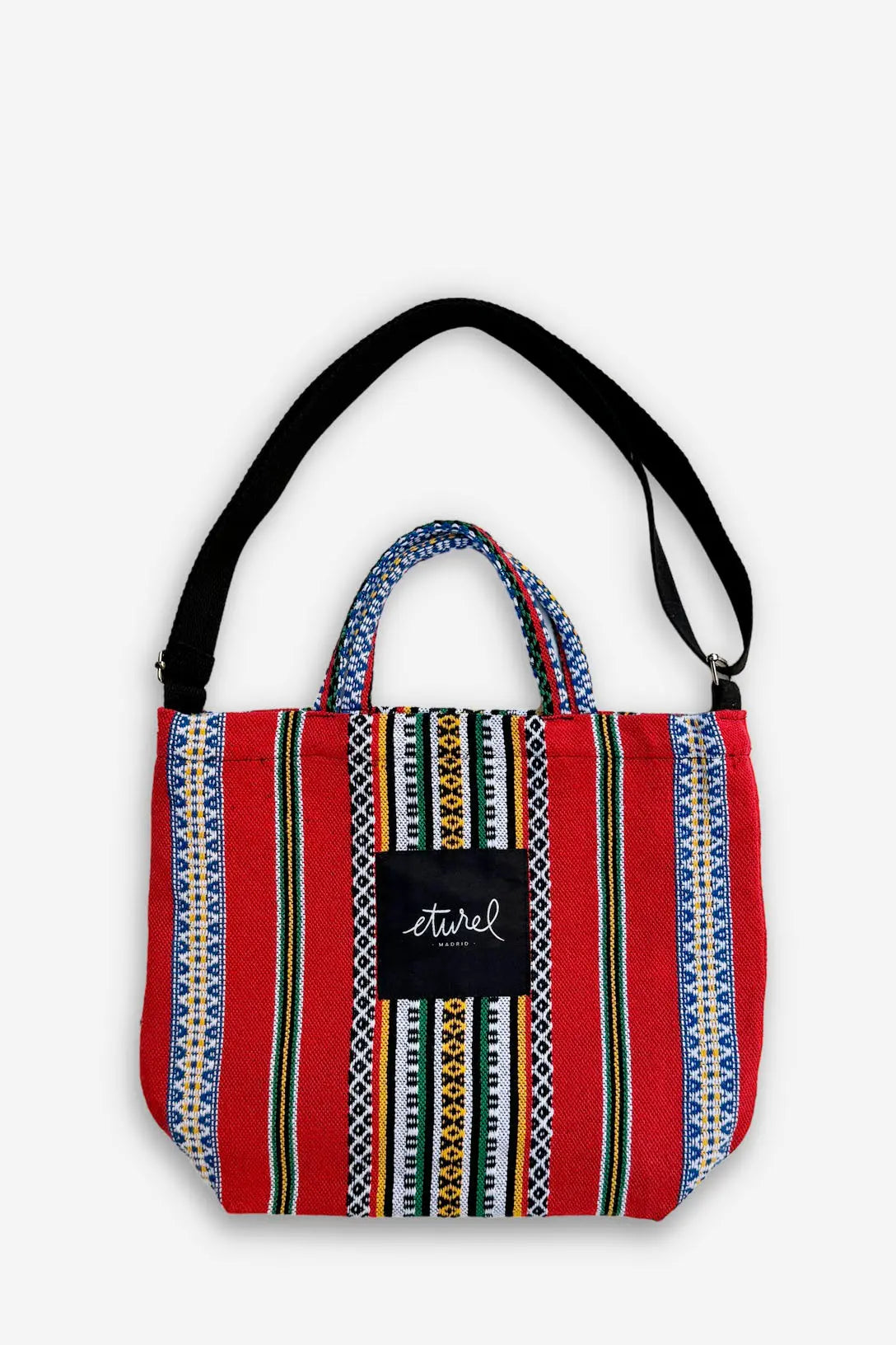 Bolso bandolera de tela roja con rayas multicolores, asas cortas y correa negra ajustable sobre fondo blanco.