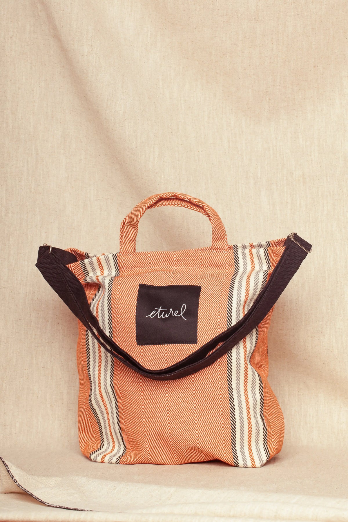Bolso bandolera de sarga color arcilla con patrón de rayas y tejido texturizado sobre fondo de lino neutro.