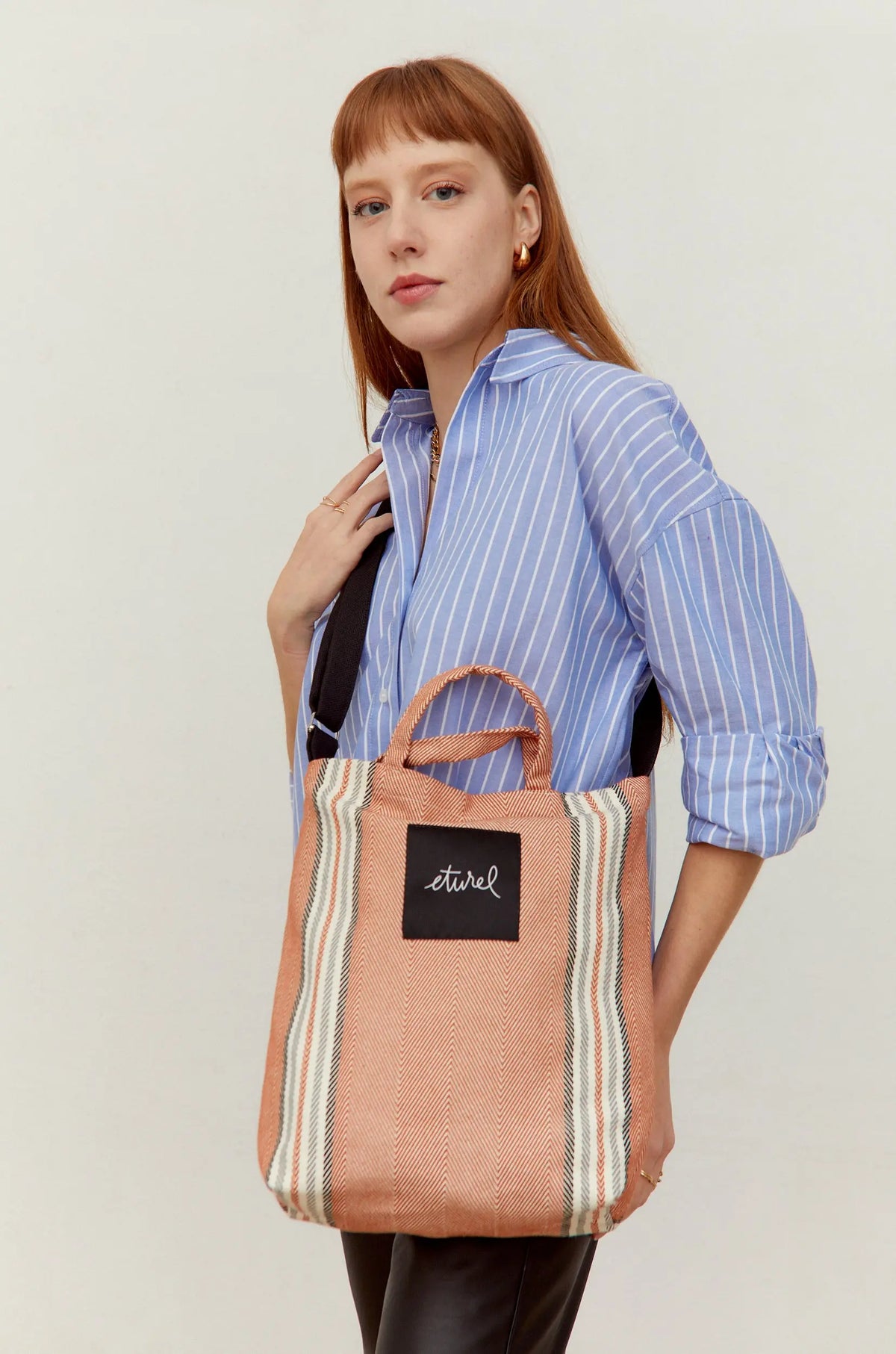 Bolso bandolera de sarga en color arcilla con rayas verticales y correas negras, lucido por una modelo.