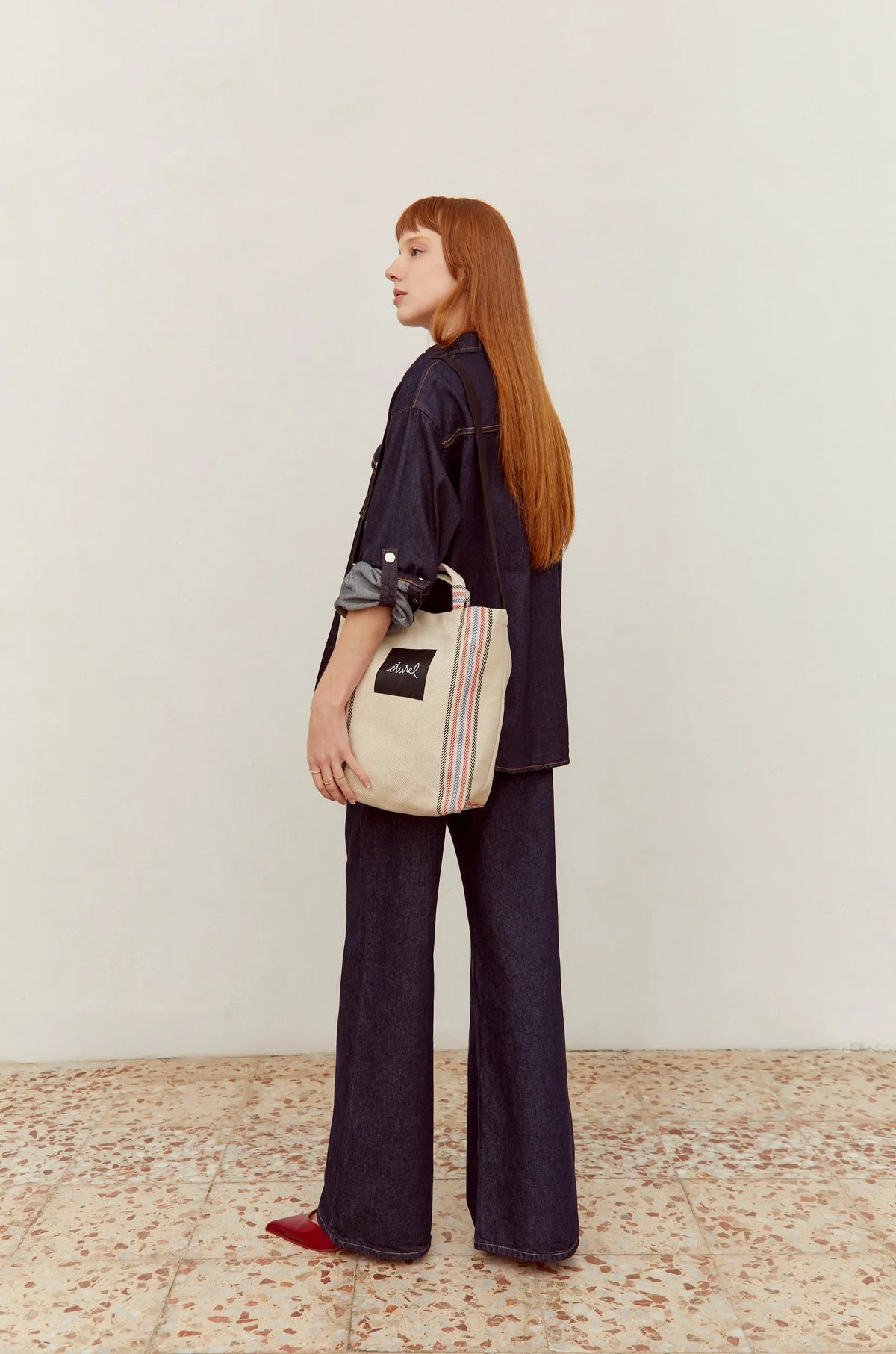 Bolso bandolera de sarga color crudo con detalle de franjas laterales y asas, llevado por una mujer con look denim.