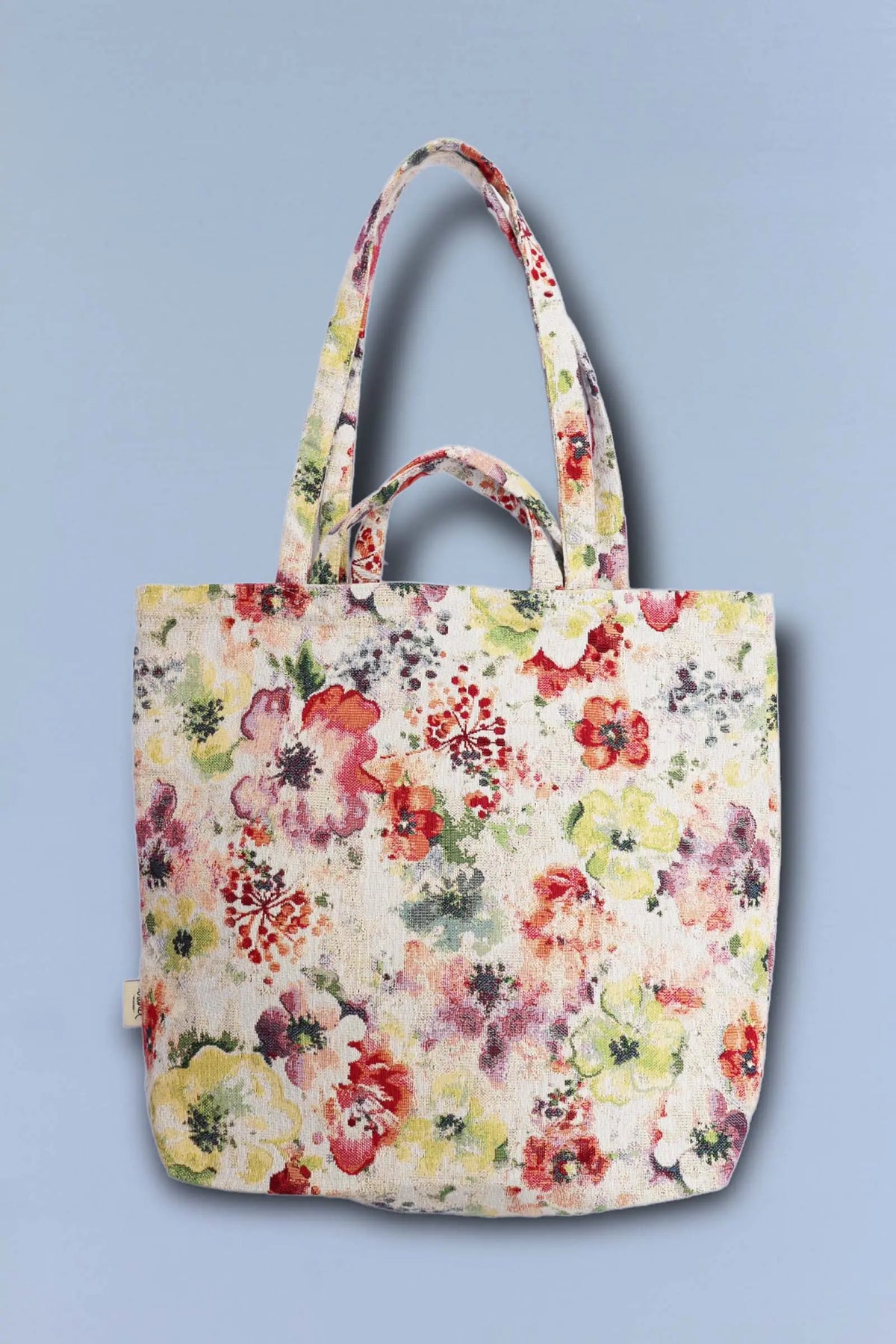 Jacquard tote bag featuring a vibrant, multicolored poppy floral print on a cream background with double handles.
