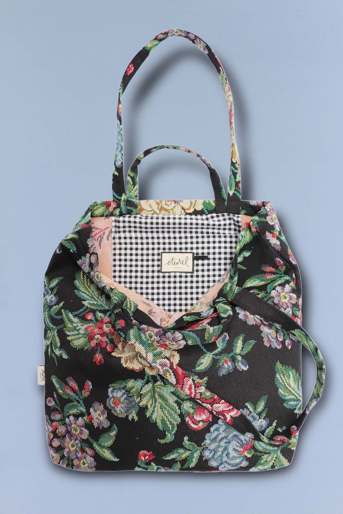 Tote bag de tejido jacquard con estampado de peonías sobre fondo negro y forro interior de cuadros vichy blanco y negro.