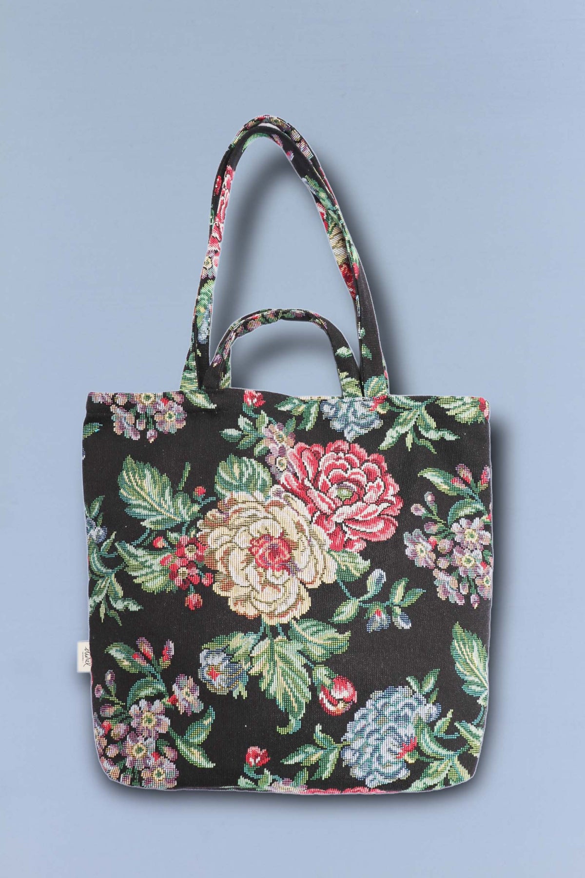 Tote bag de tela jacquard con estampado floral de peonías en tonos rojos y cremas sobre fondo negro.