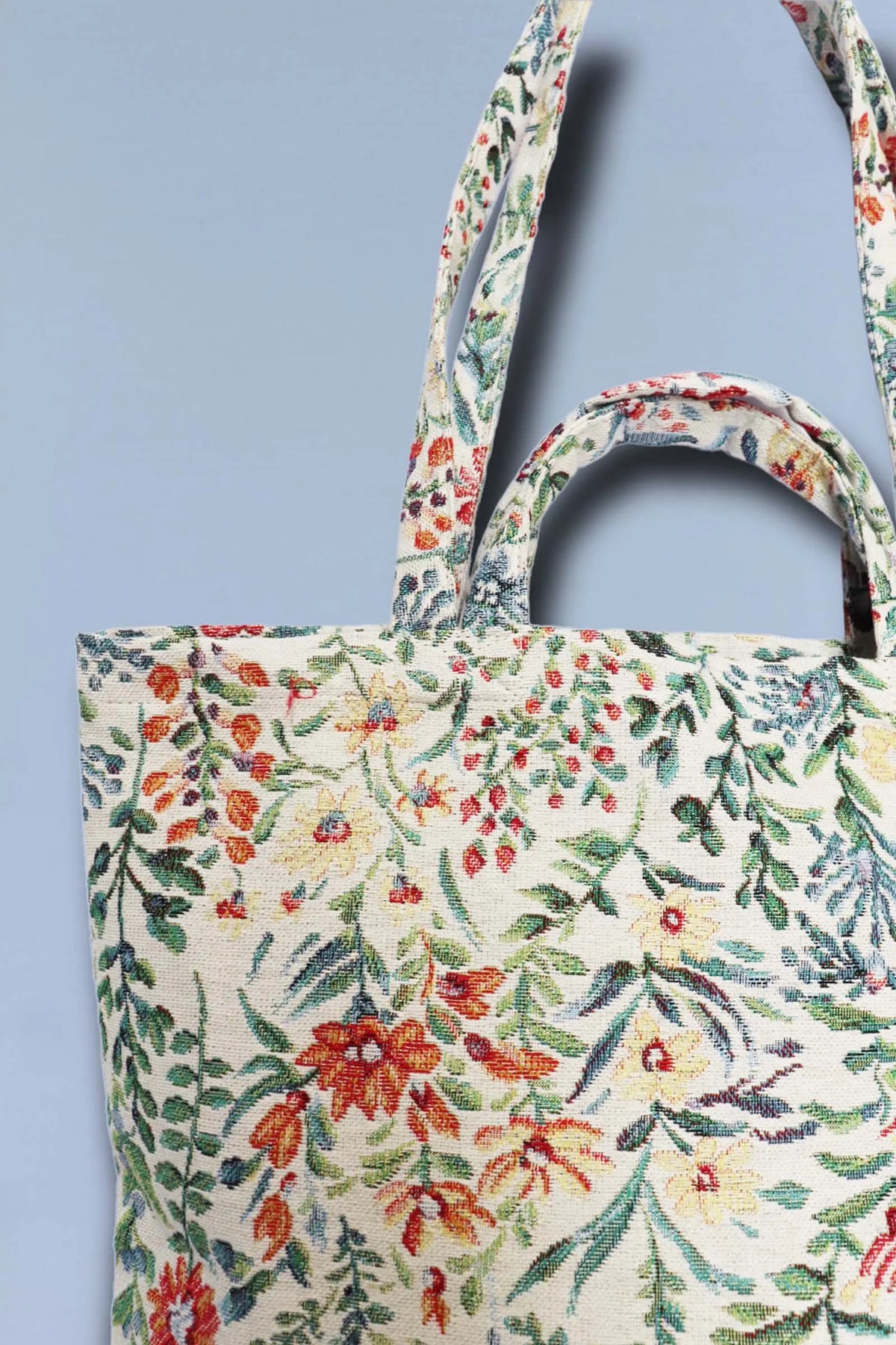 Tote bag de tela jacquard con estampado floral de azaleas en tonos vivos, fondo claro y asas reforzadas.