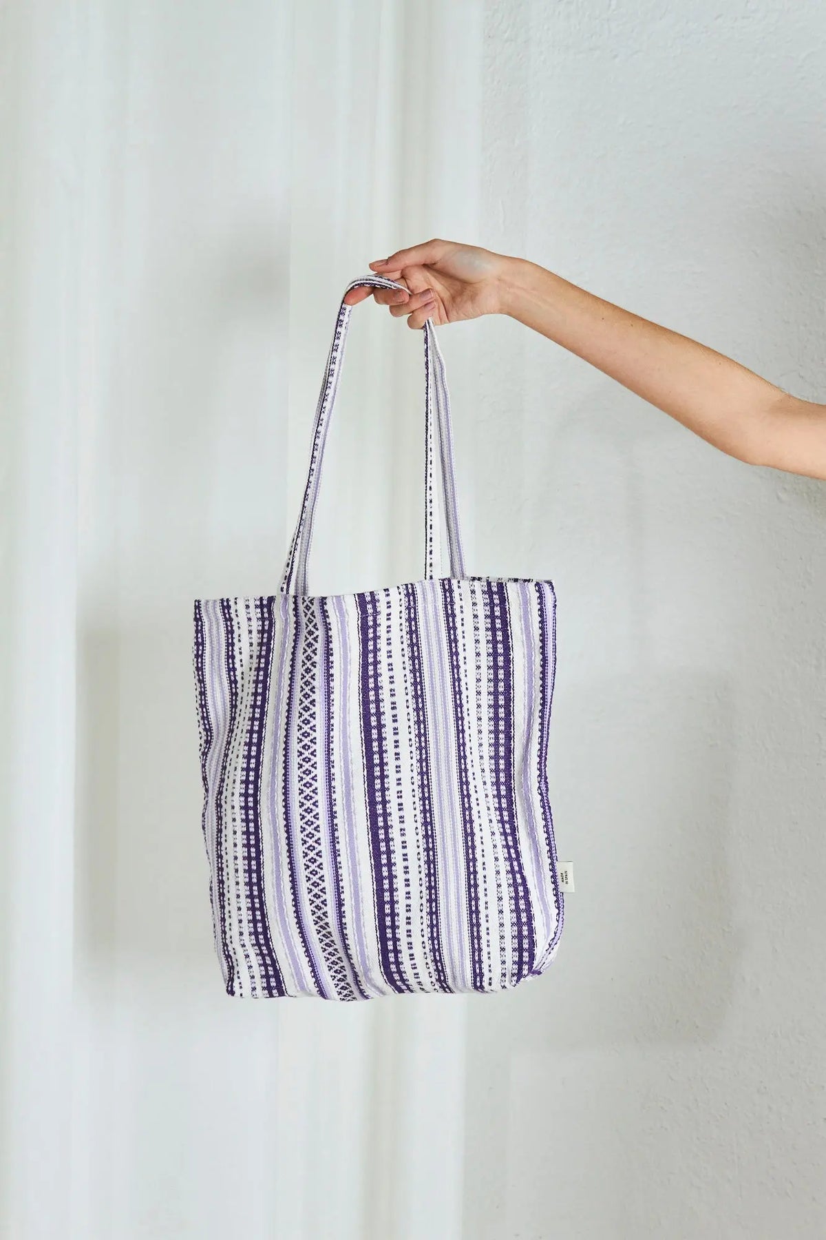 Handheld fabric tote bag in woven mauve and white striped geometric patterns with long shoulder straps.