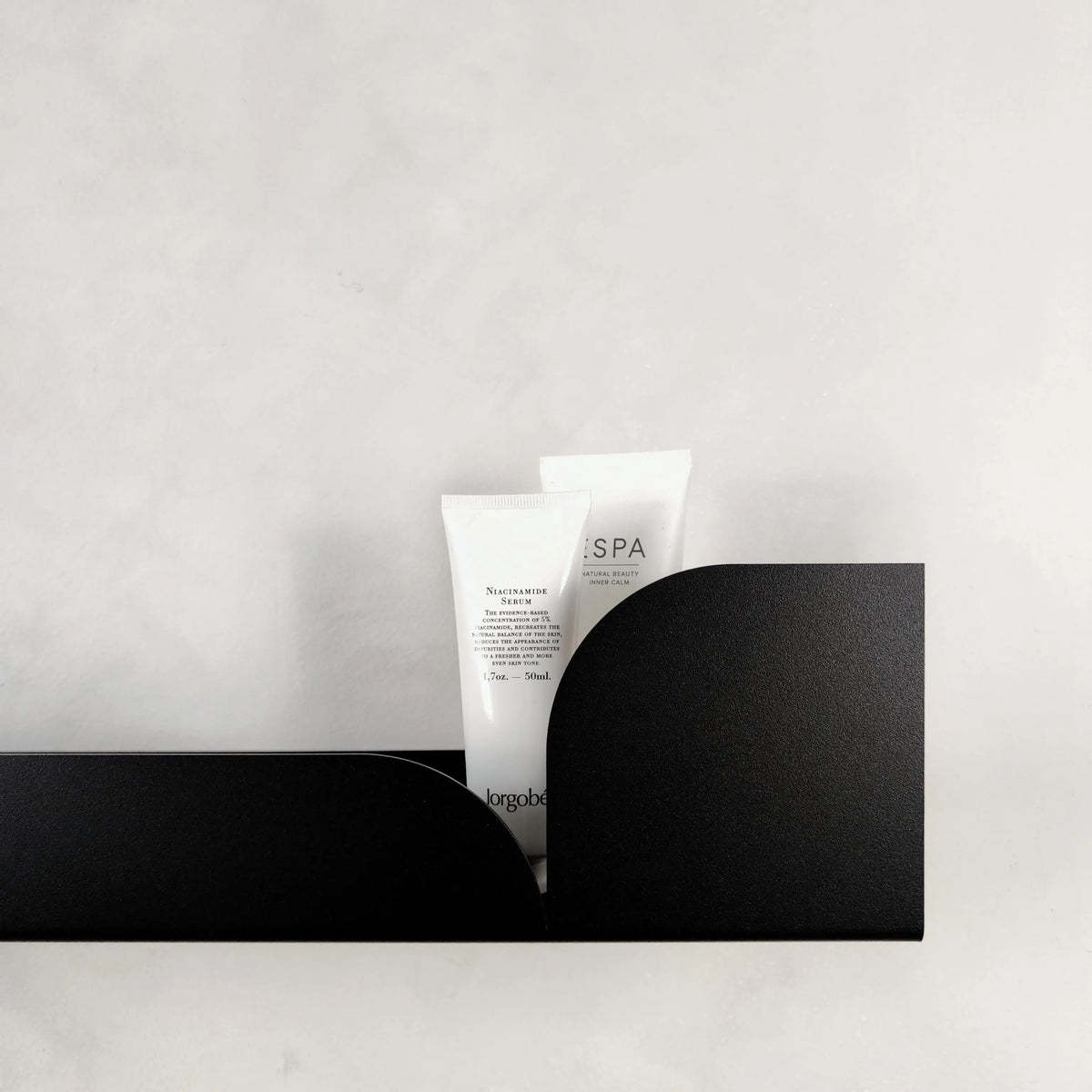 Estante flotante de metal negro con diseño curvo minimalista, ideal para organizar productos de cuidado personal.