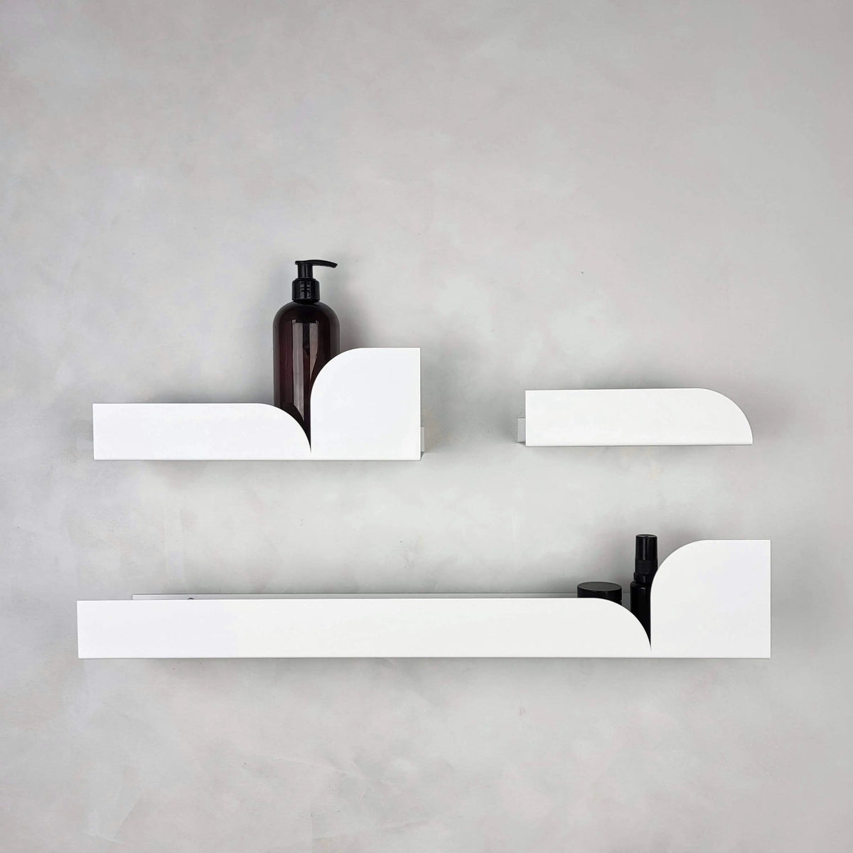 Estantes flotantes metálicos de color blanco con diseño minimalista y formas curvas, fijados sobre una pared gris.