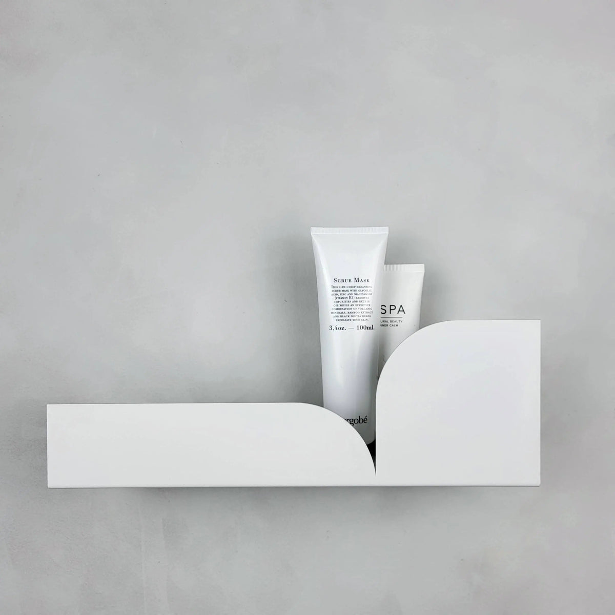 Estante flotante de metal blanco con diseño minimalista curvo sobre pared gris, sosteniendo tubos de productos de aseo.
