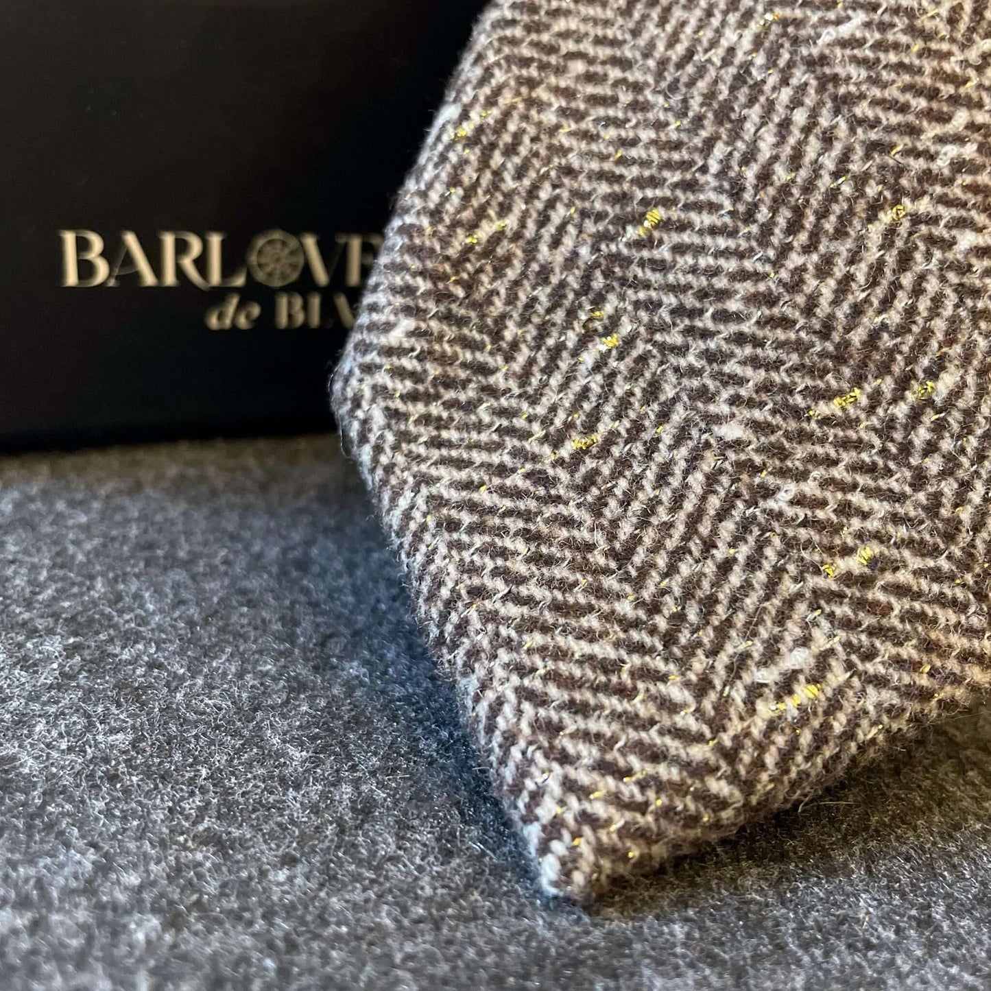 Corbata de lana marrón con patrón de espiga y detalles de hilo dorado brillante. Textura gruesa y estilo clásico.
