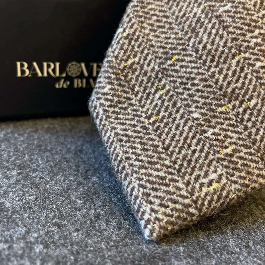 Corbata de lana marrón con patrón de espiga y detalles de hilo dorado brillante. Textura gruesa y estilo clásico.