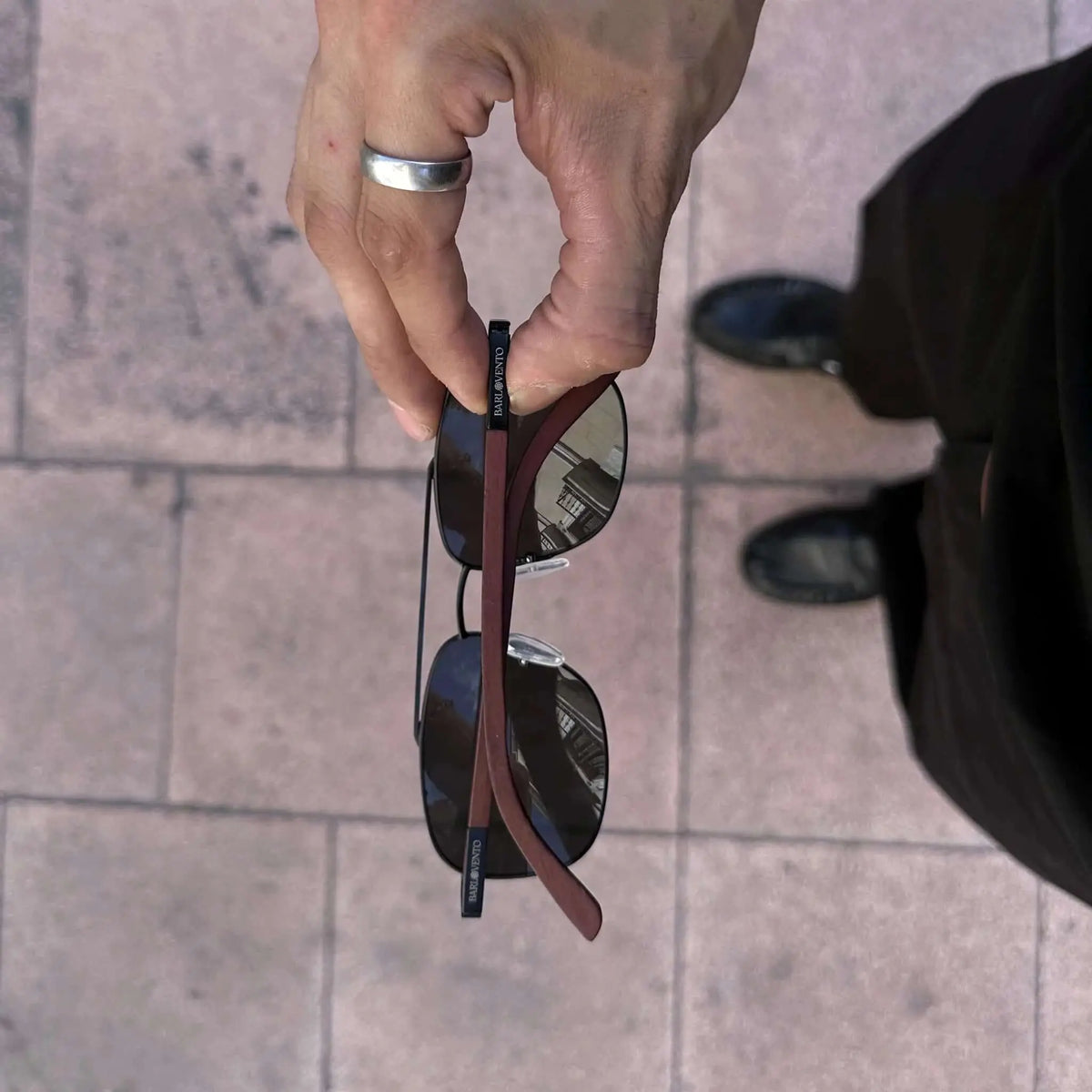 Gafas de sol con montura negra, cristales oscuros y patillas de madera marrón oscuro. Estilo casual y moderno.