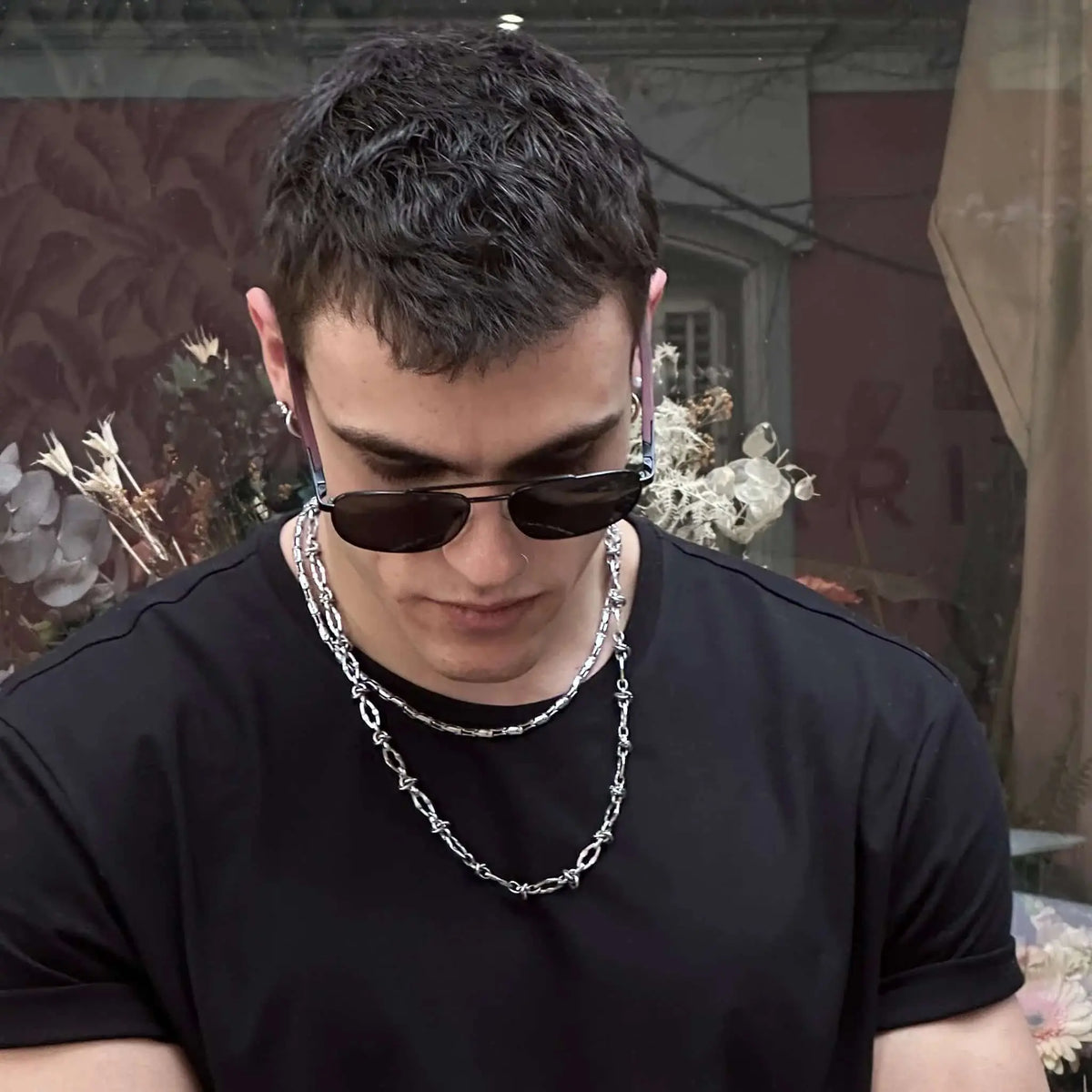 Gafas de sol estilo aviador con cristales oscuros y patillas de madera grabadas, puestas por un hombre con cadena.
