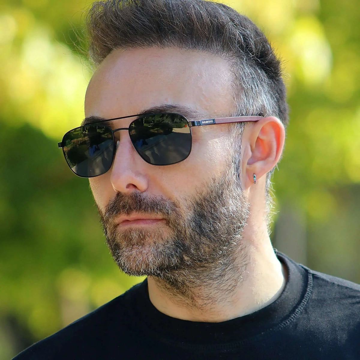 Gafas de sol estilo aviador con montura metálica negra y patillas de madera, lucidas por un hombre con barba.