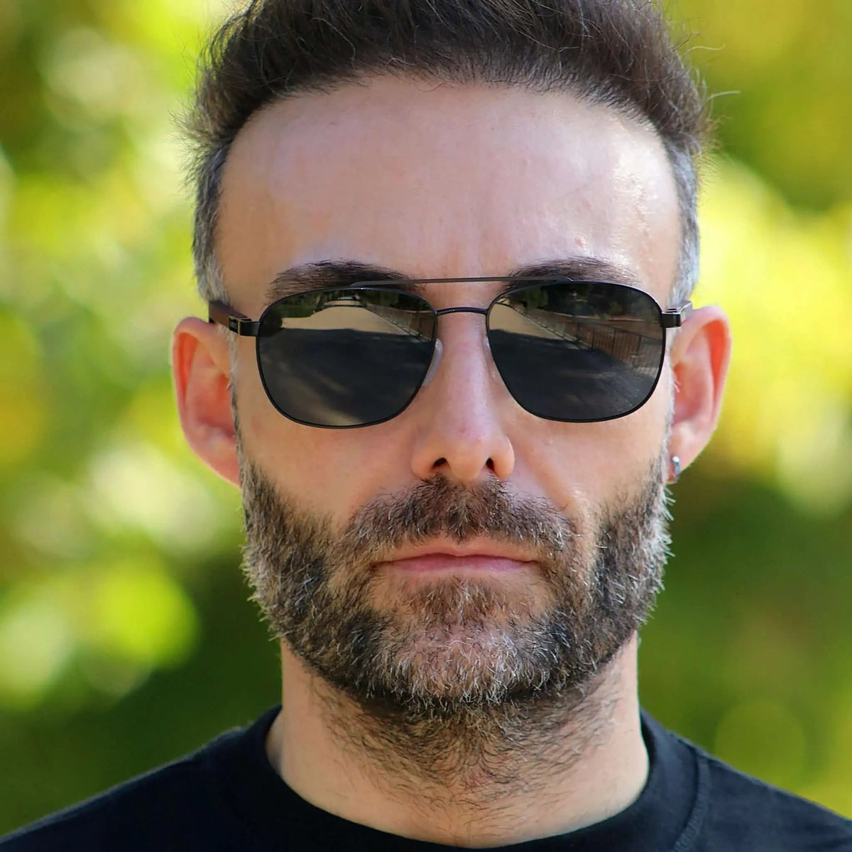 Gafas de sol estilo aviador con montura metálica oscura, cristales oscuros y patillas de madera sobre hombre barbudo.