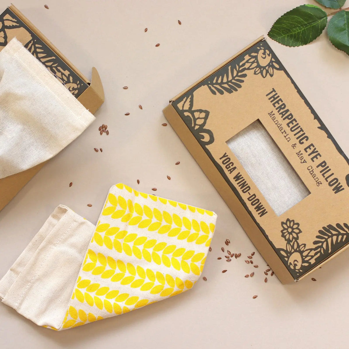 Almohada rectangular de tela con estampado de hojas amarillas, junto a su caja de cartón artesanal con semillas.