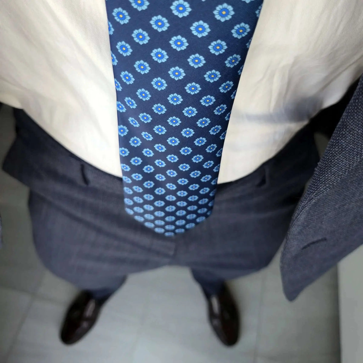 Corbata azul marino con estampado floral celeste sobre camisa blanca y traje gris estructurado.