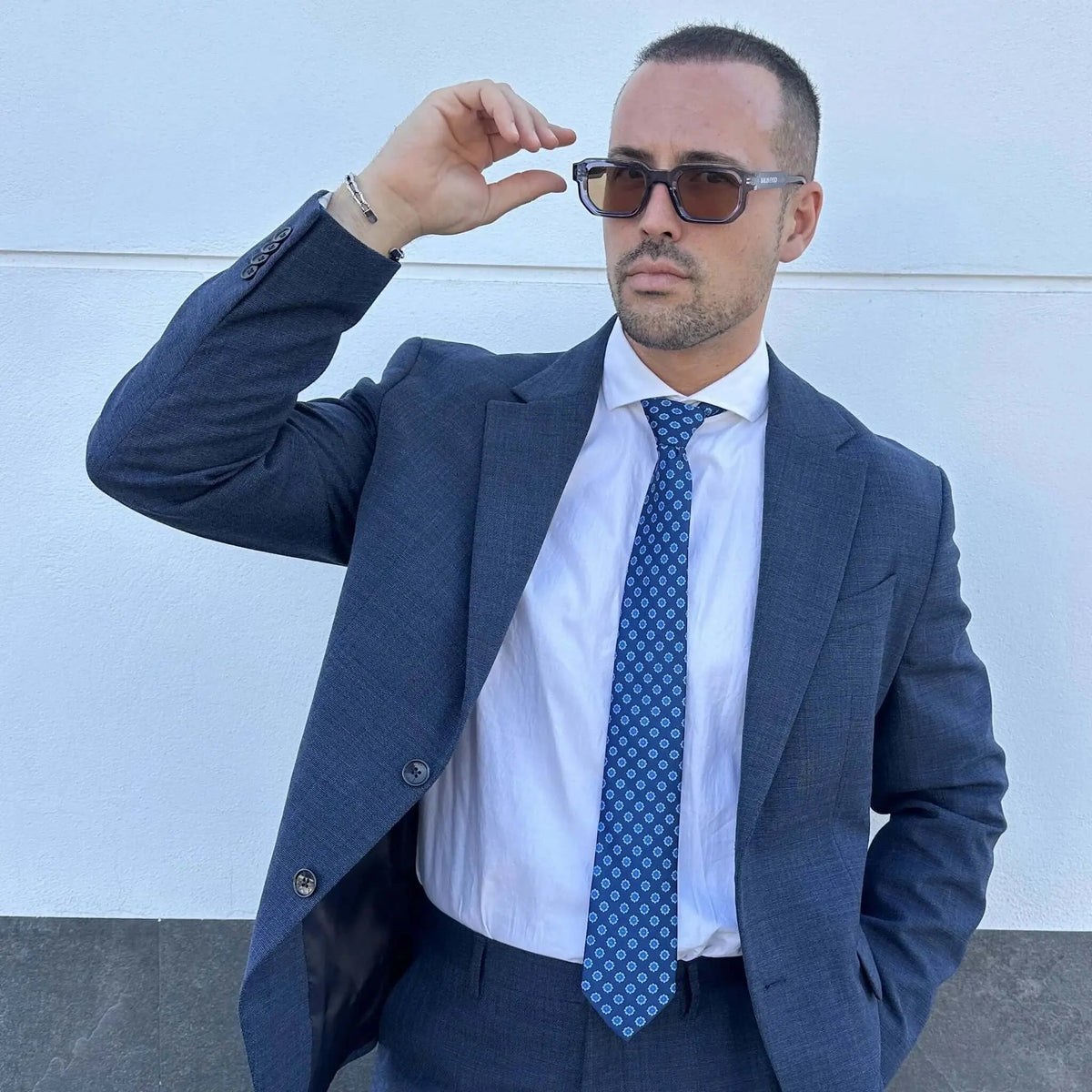 Hombre con traje azul y camisa blanca, luciendo una corbata azul marino con estampado geométrico pequeño.