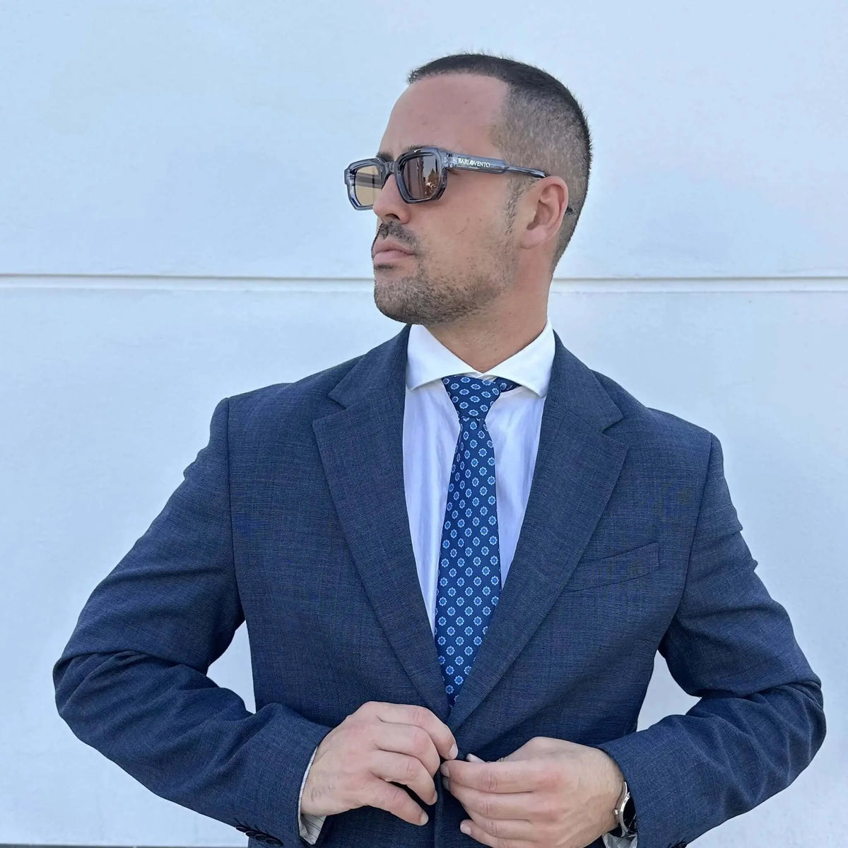 Hombre con traje azul, camisa blanca y corbata azul marino con estampado de rombos pequeños en tono claro.