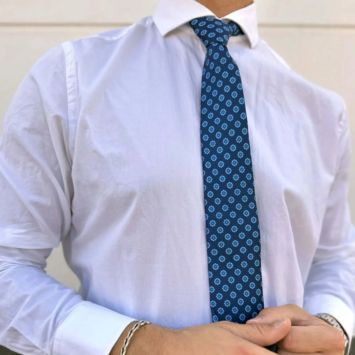 Corbata azul marino con estampado de pequeñas flores blancas y azules, sobre camisa blanca de vestir.