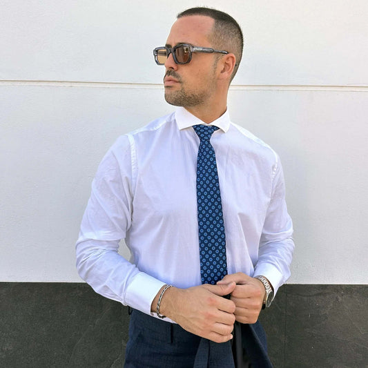 Hombre con camisa blanca y corbata azul marino con estampado geométrico pequeño, estilo formal y elegante.