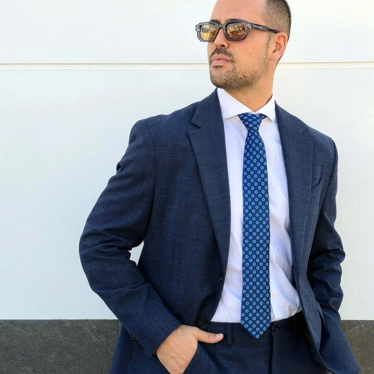 Hombre con traje azul, camisa blanca y corbata azul con patrón geométrico estilo italiano.