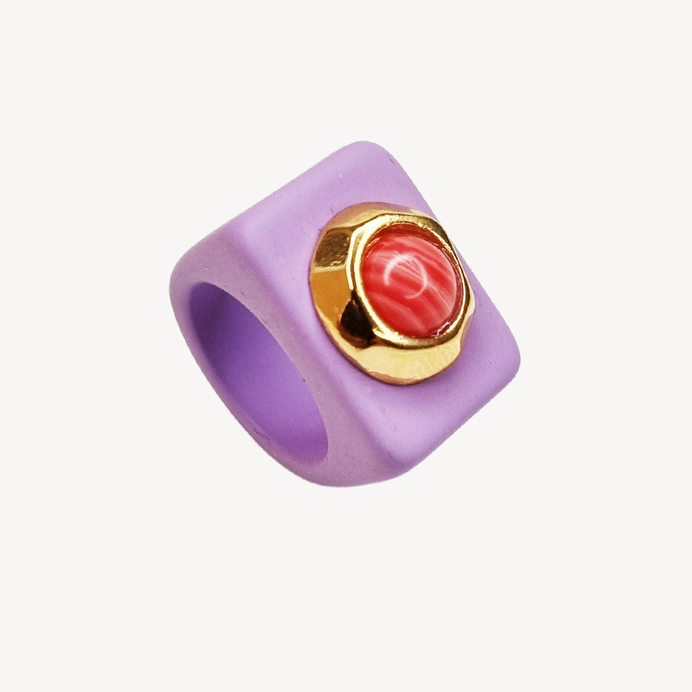 Anillo cuadrado de goma lila con detalle dorado y piedra coral. Estilo moderno y atractivo.