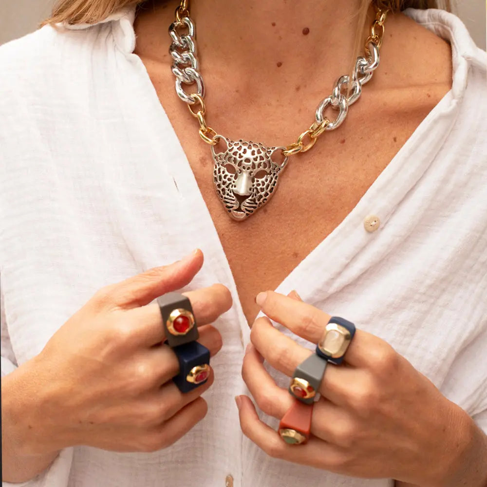 Collar de leopardo dorado y plateado con cadenas, anillos de colores azul, gris y naranja, estilo moderno y audaz.