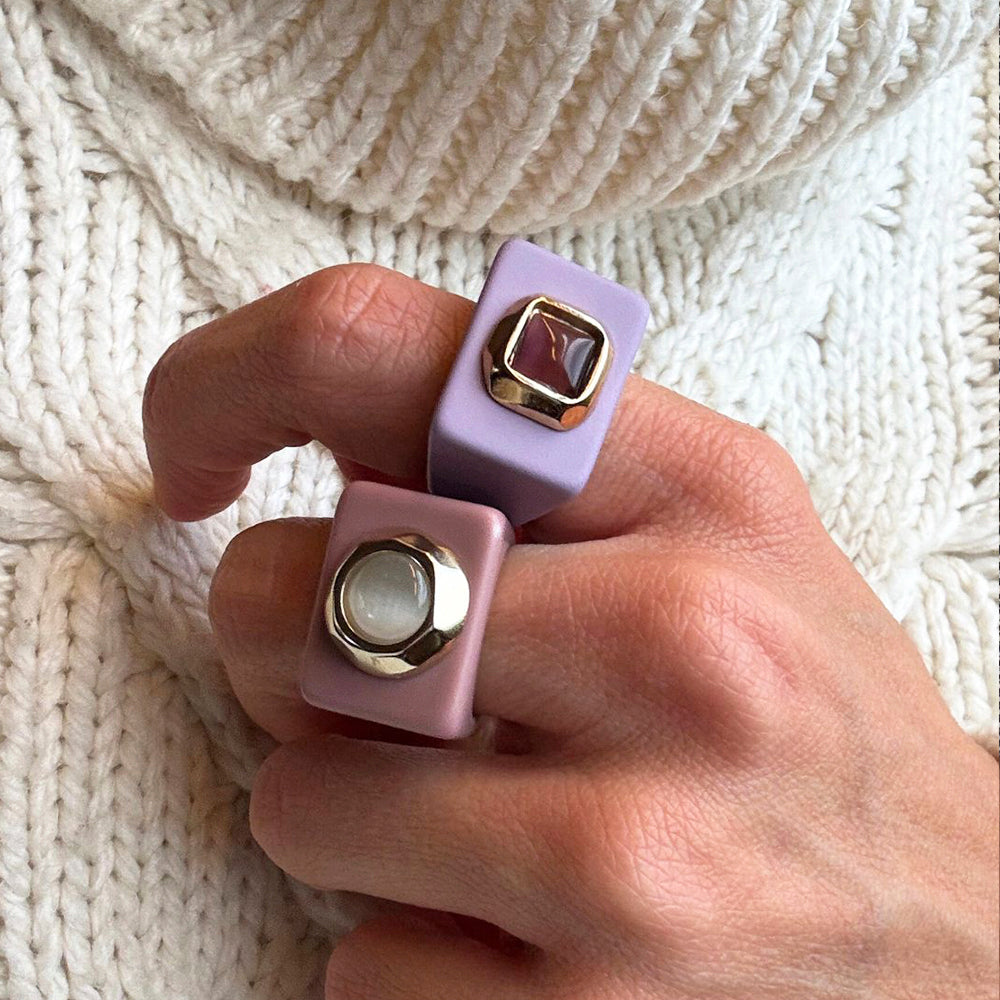 Anillo cuadrado de cerámica lila y rosa con detalles metálicos, estilo moderno y elegante.
