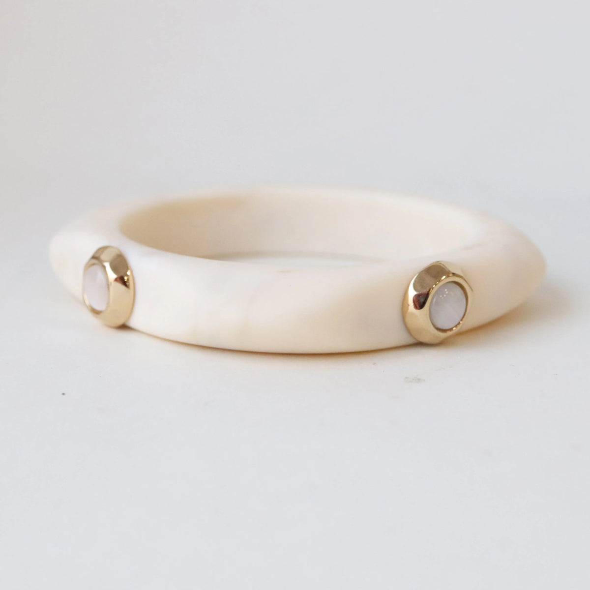 Pulsera de resina blanca con detalles dorados y piedras pink, diseño moderno y elegante.