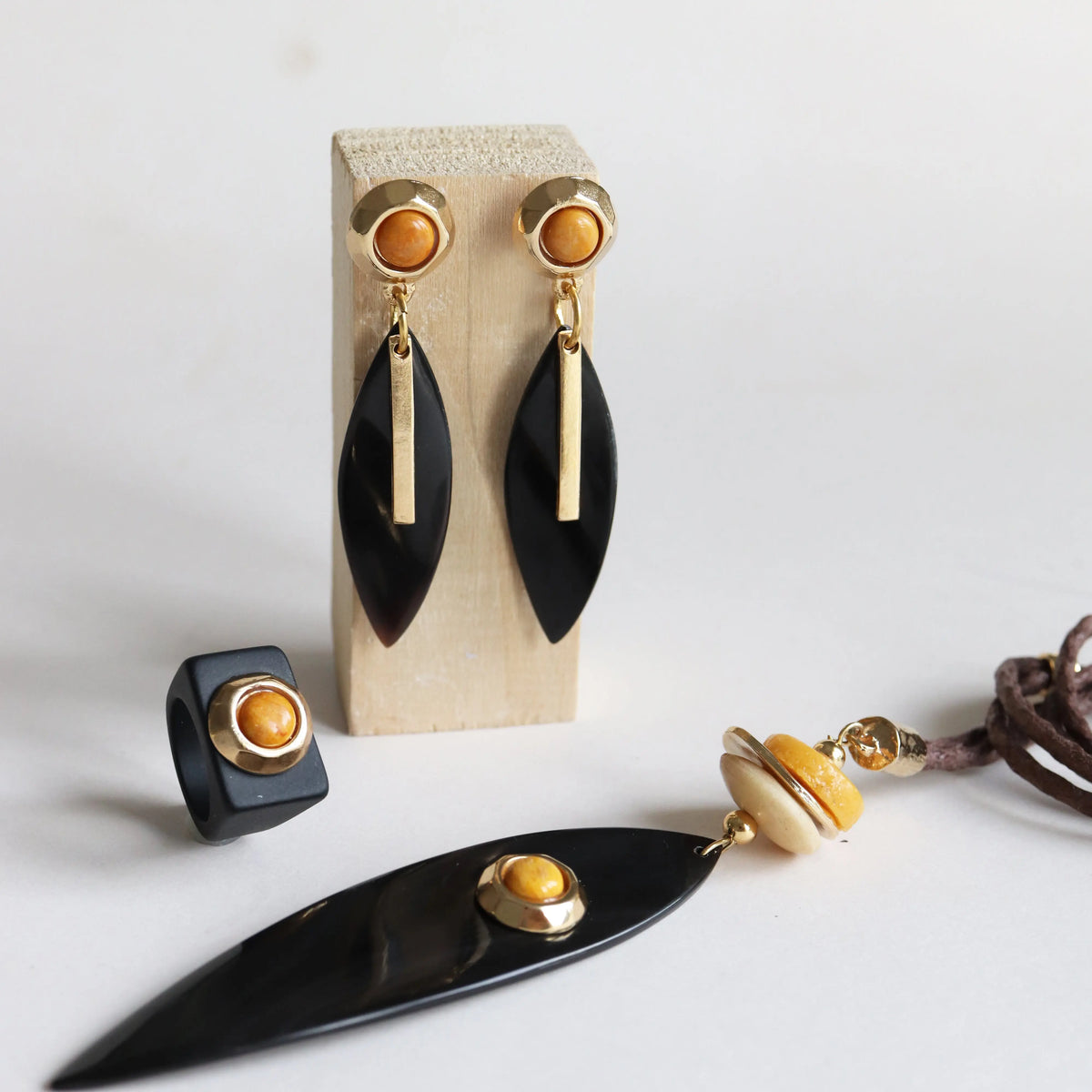 Pendientes negros con detalles dorados y anillo negro, collar con cuentas de madera y cuero, estilo moderno.