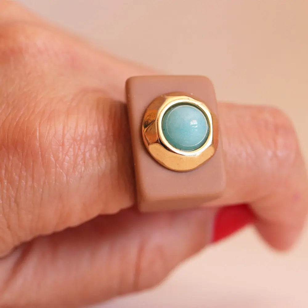 Anillo de resina beige con piedra azul y detalle dorado, diseño moderno y elegante.