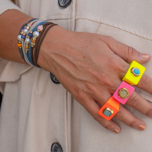 Anillo neon rosa y amarillo con detalles dorados, combinado con pulseras de cuero y perlas.