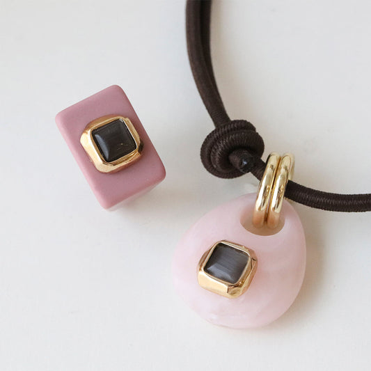 Collar de arcilla rosa y marrón con adornos dorados y piedras grises, estilo moderno y elegante.