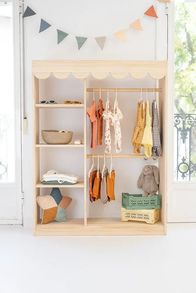 Estante de madera claro con ropa infantil en tonos mostaza y terracota, decoración colorida y estilo minimalista.