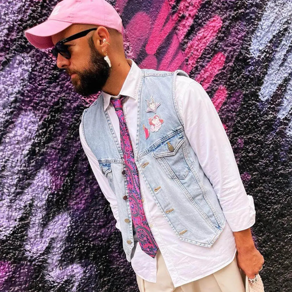 Corbata rosa con estampado paisley sobre camisa blanca, chaleco de mezclilla claro y accesorios coloridos.