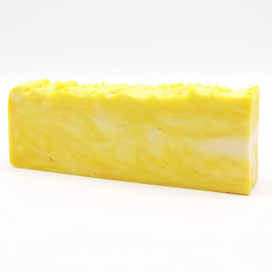 Barra de jabón artesanal rectangular, de color amarillo vibrante con veteados blancos y textura superior rugosa.